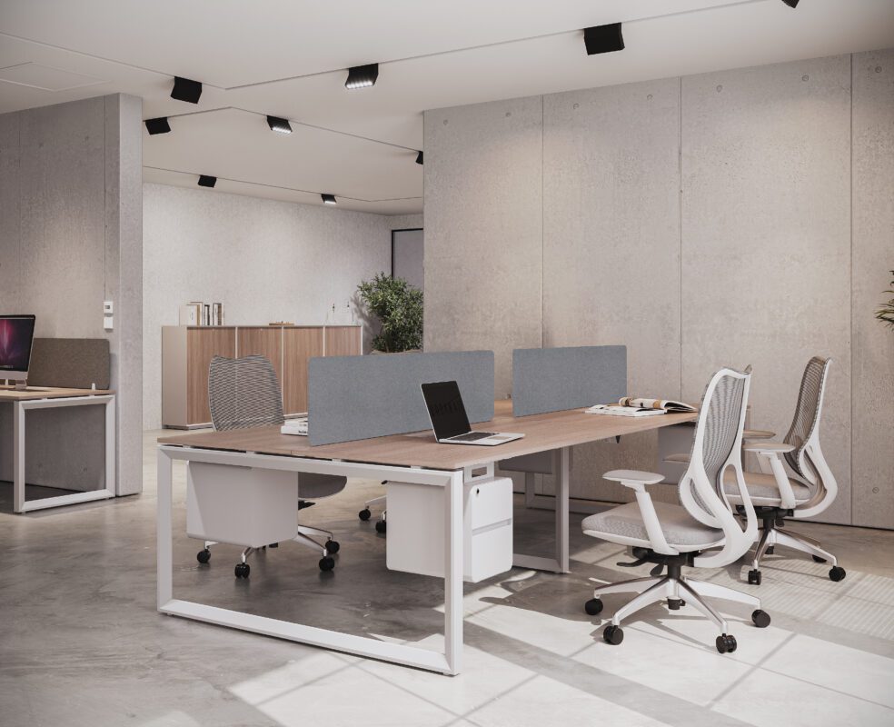 Spacious and bright modern office workstation featuring a long light wood desk with white legs, offering multiple seating areas separated by gray privacy panels.