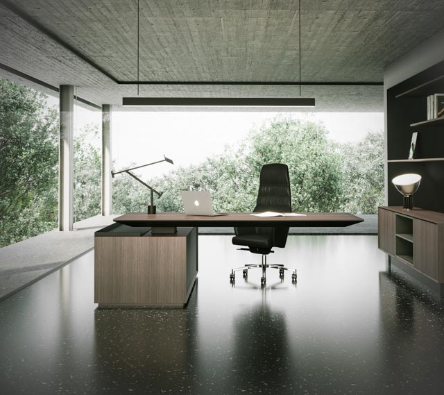 Sleek, modern executive desk with a dark wood finish and asymmetrical return, situated in a minimalist office space featuring concrete architecture and floor-to-ceiling windows overlooking dense greenery.