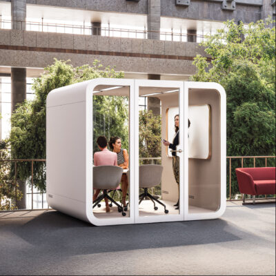 Modern modular meeting pods with glass walls installed in an open atrium area surrounded by greenery. Office Pod showing a small business meeting in progress inside one unit.